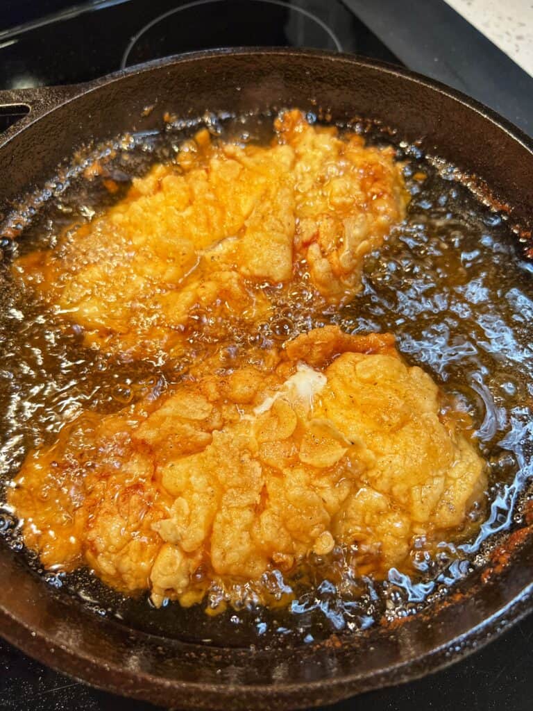 Chicken breasts frying in a cast iron pan ready to be flipped.