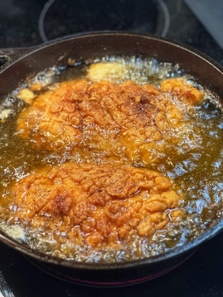 Two pieces of browned and crispy chicken done frying in a cast iron pan.