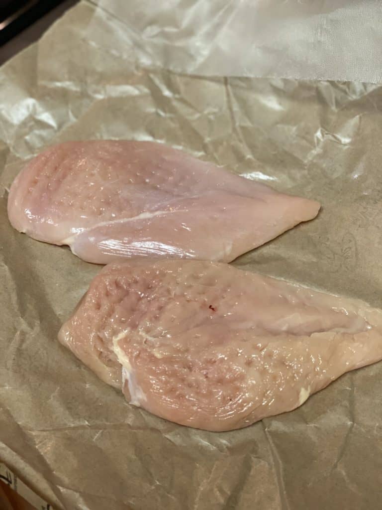 Two flattened chicken breasts laying on a brown piece of butcher